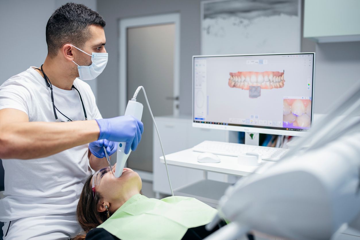 male dental technician scanning a female dental patient's teeth while viewing the scan on a nearby m