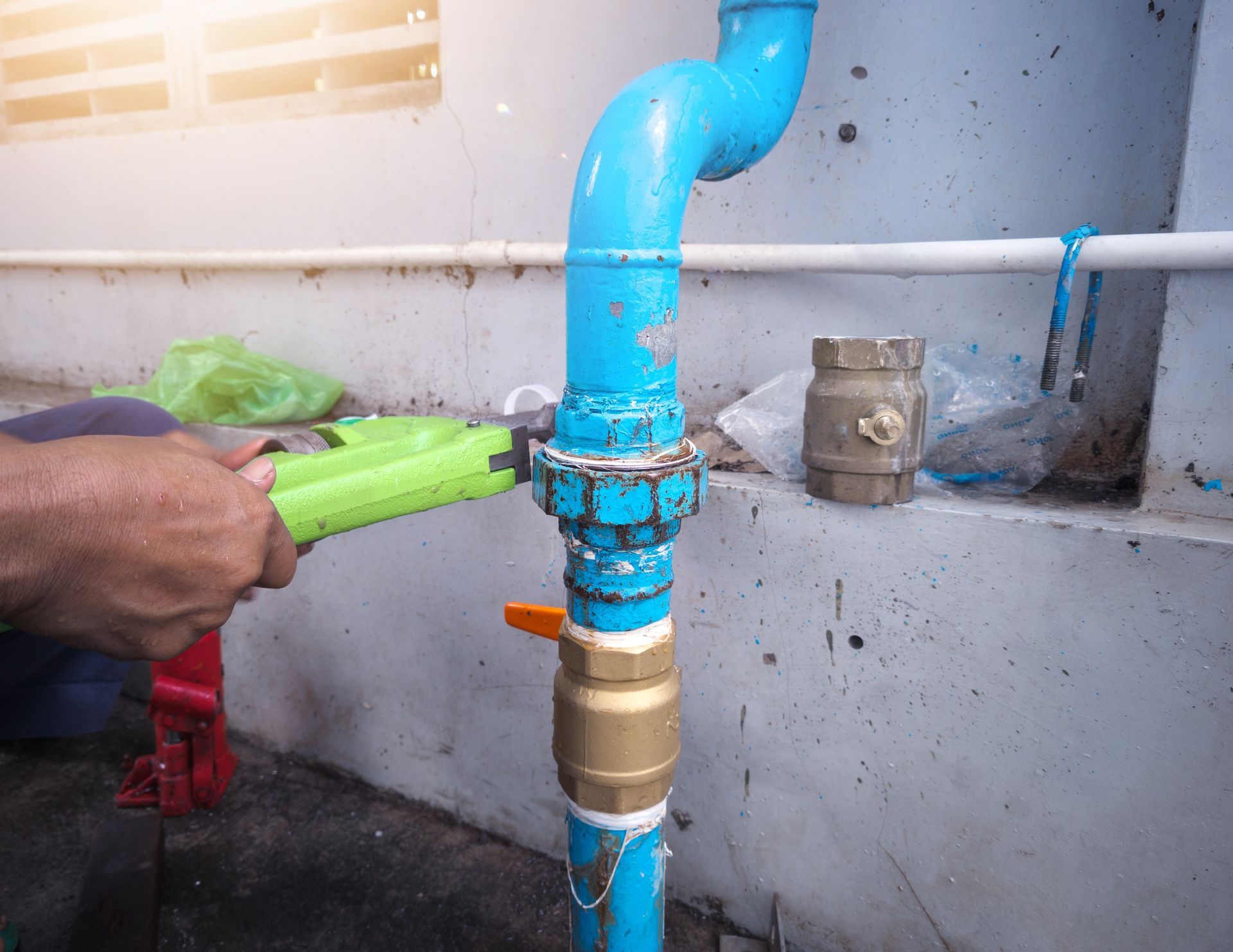 Plumber tightening a blue water pipe fitting with a large wrench during plumbing repair work. Plumber tightening a blue water pipe fitting with a large wrench during plumbing repair work.