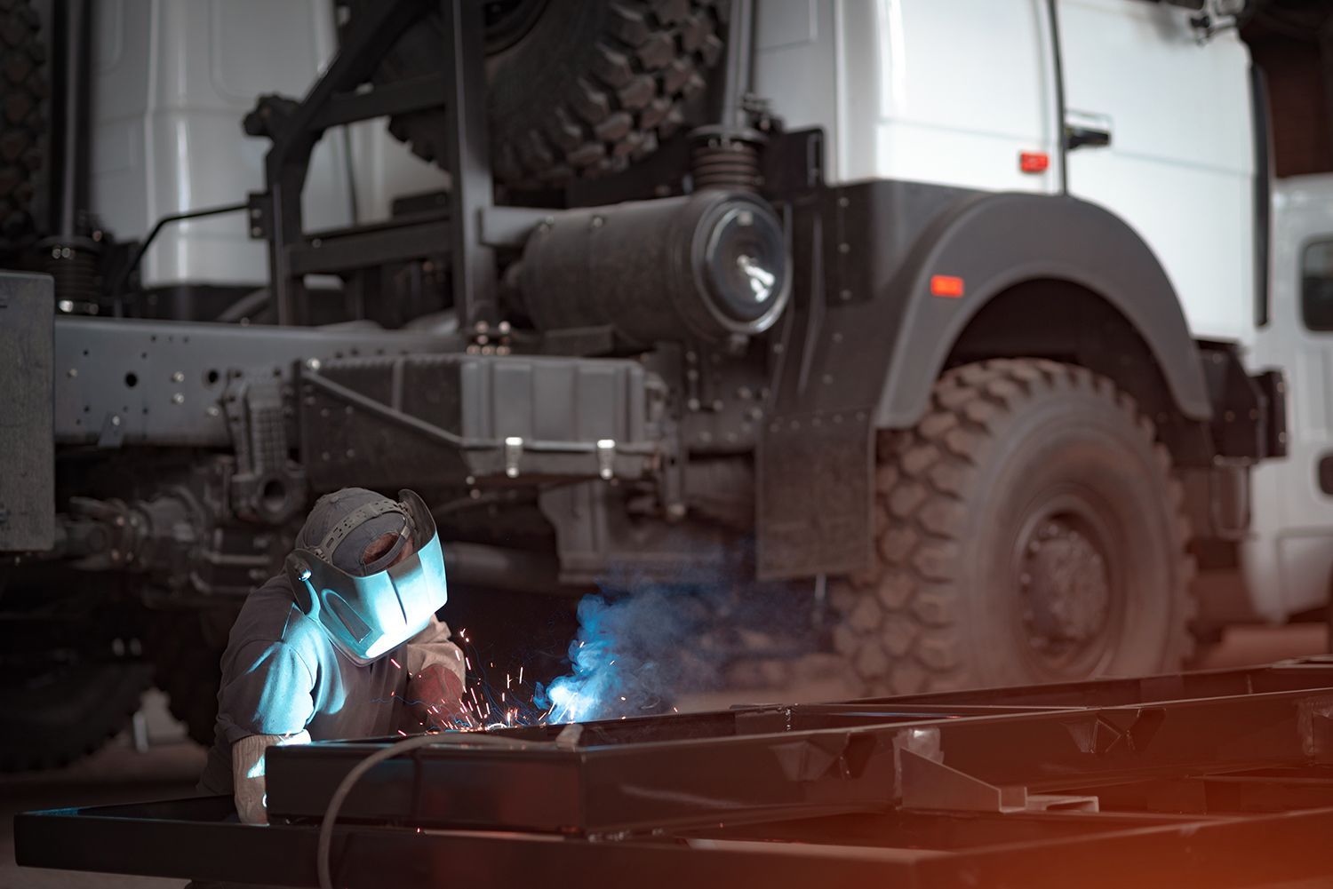A welder in a car workshop welds a truck frame.