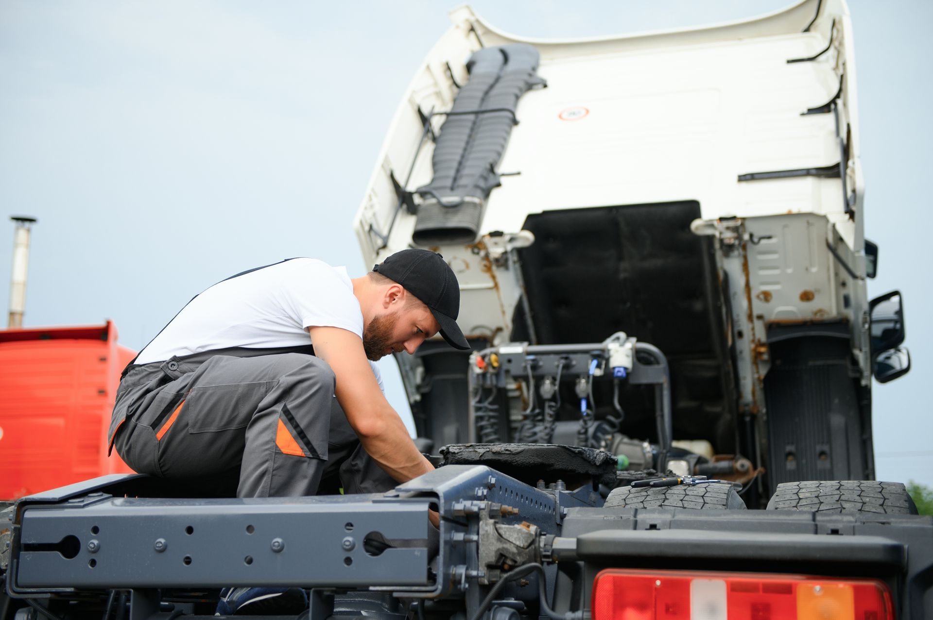 Mechanic working on the chassis of a trailer truck with the cab lifted for repairs.