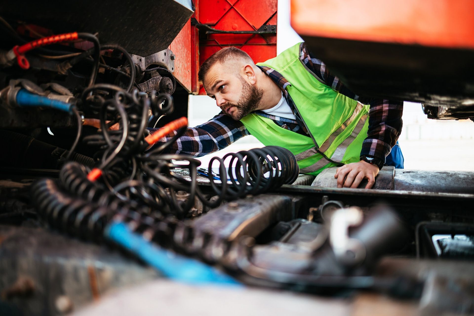 Mechanic inspecting truck engine components and cables.
