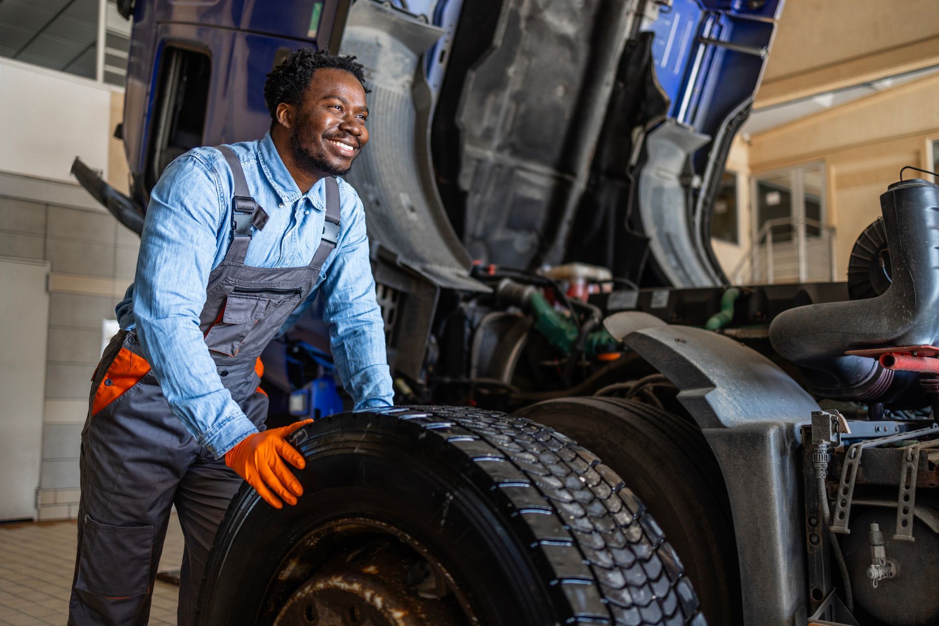 Mechanic holding a large truck tire in a repair shop.