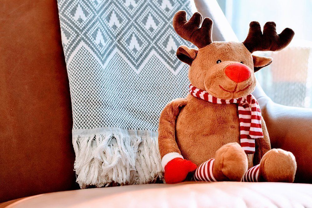 A stuffed reindeer is sitting on a couch next to a blanket.