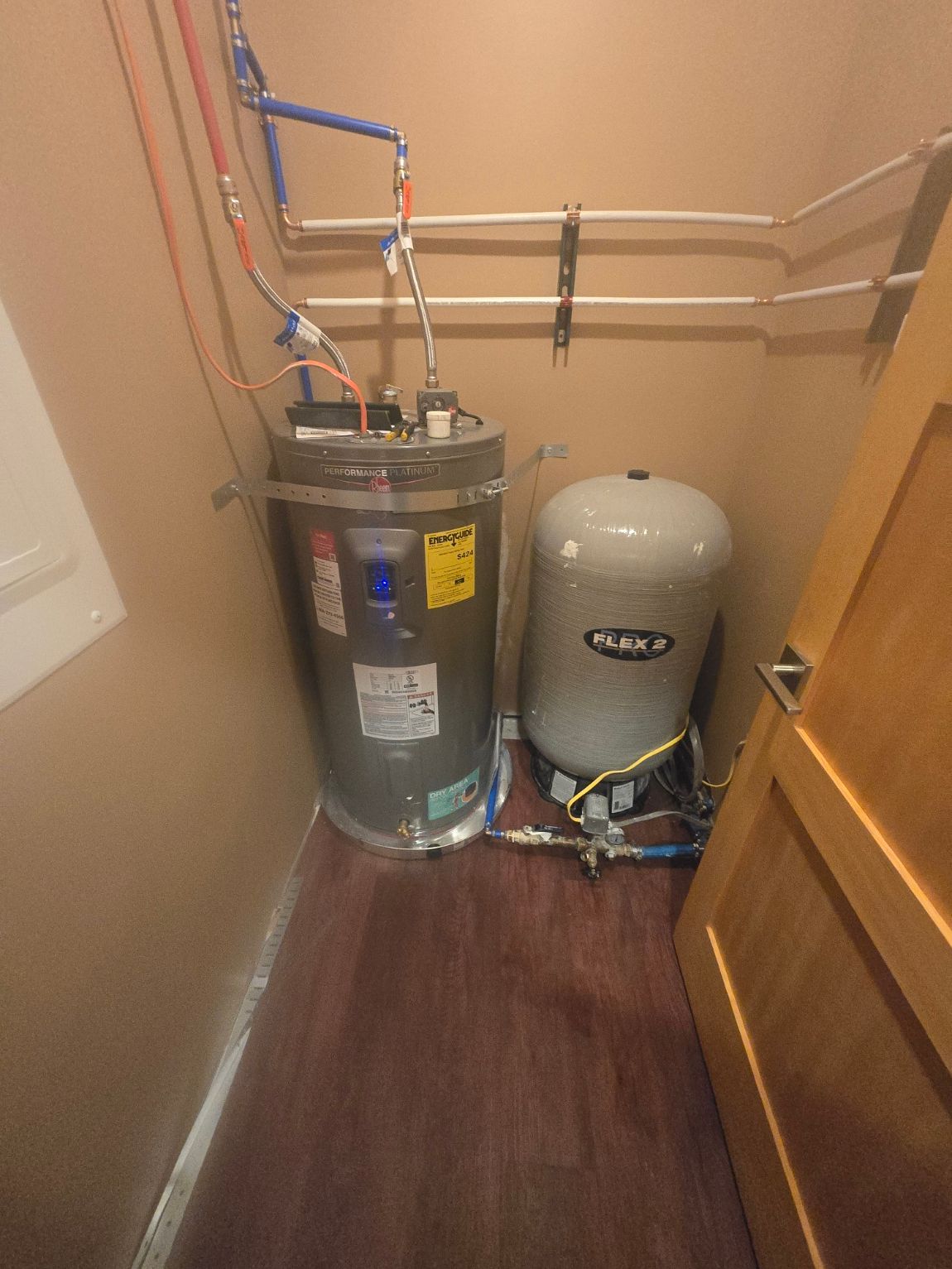 A person in work clothes installs a water heater on a white wall.