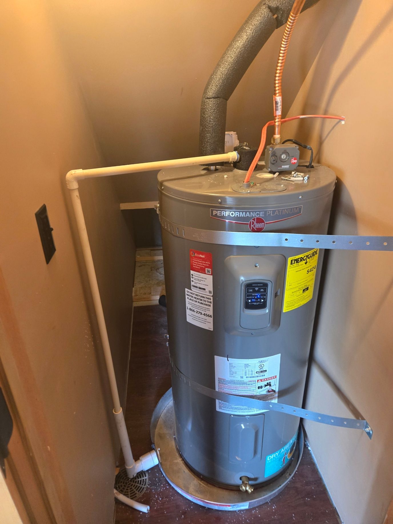 A person in work clothes installs a water heater on a white wall.