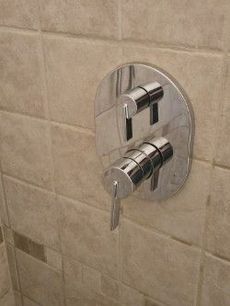 Chrome shower valve with two levers on beige tile wall.