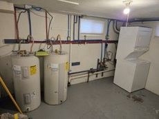Basement utility room: two water heaters, a washer/dryer, pipes along the wall, and a window.