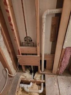 Framing with exposed plumbing and insulation during bathroom renovation.