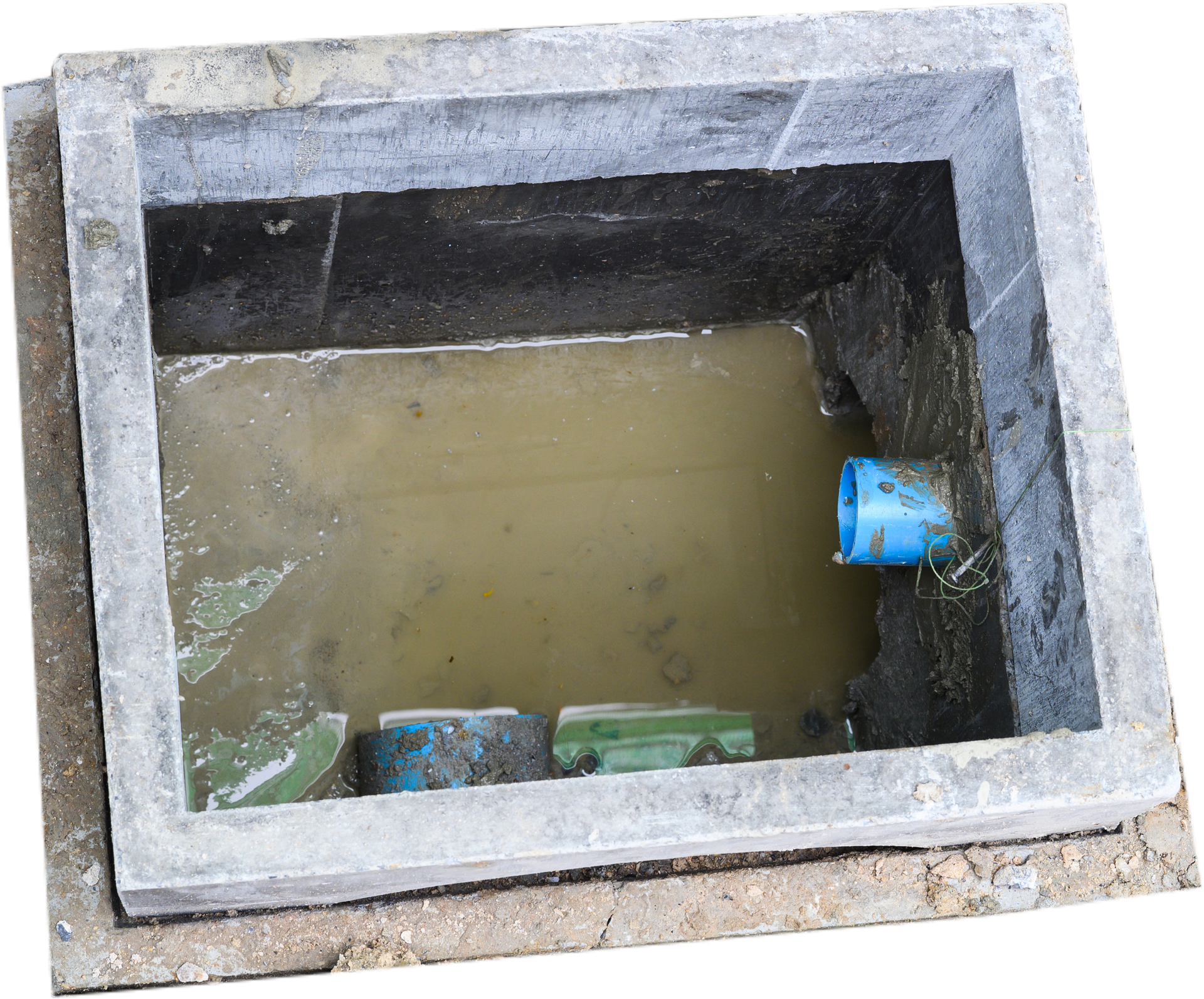 Open concrete sewer access box filled with murky water and blue pipe.