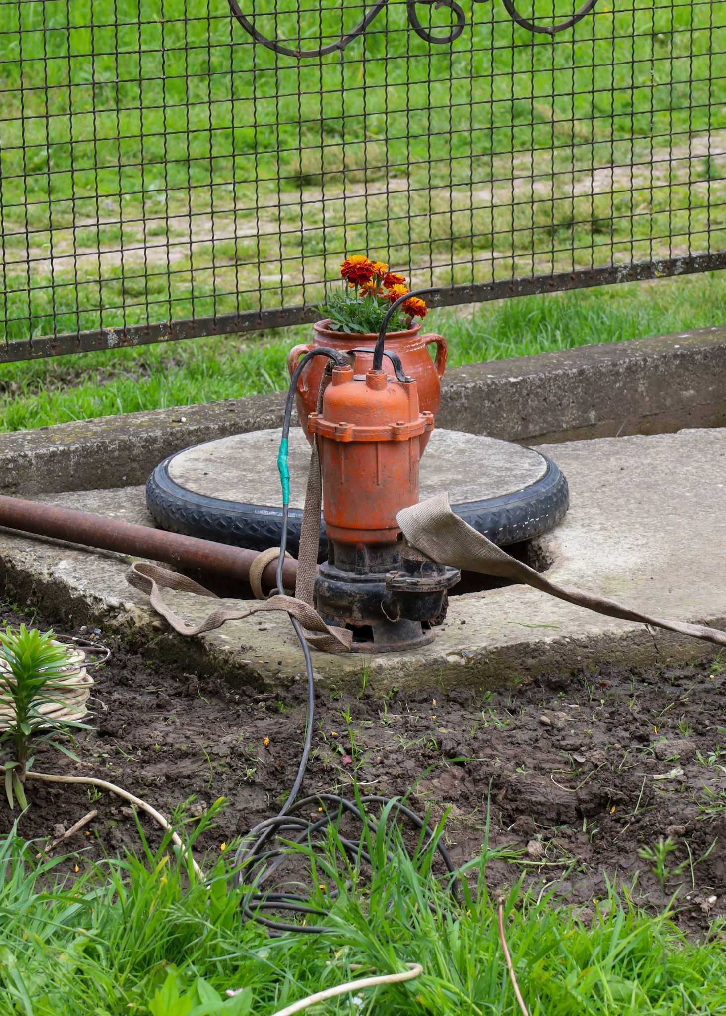 A cottage water pump and pipe stand on a concrete slab.