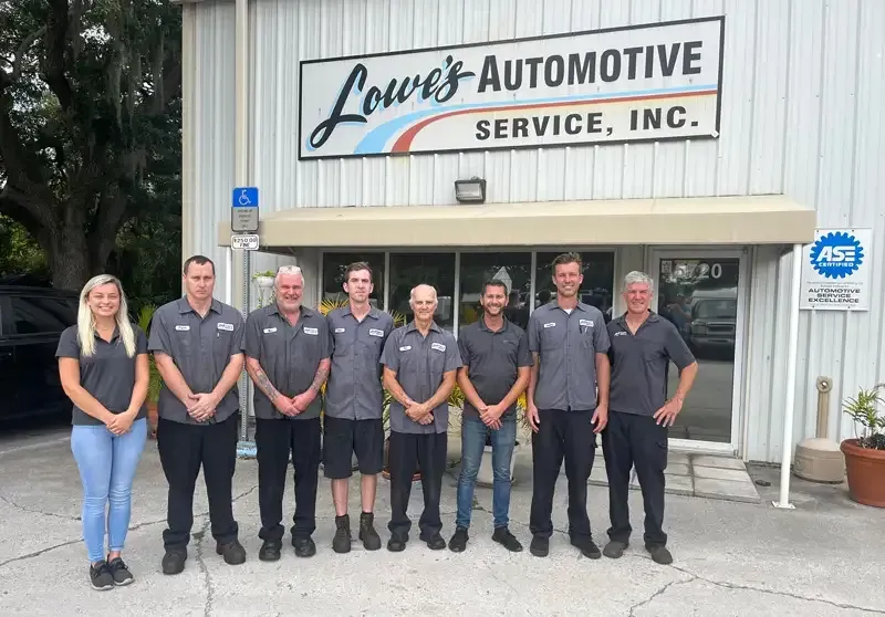Group of eight people outside Lowe's Automotive Service building. Sign above door. People wearing matching shirts.