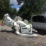 Overturned white truck with boom arm, possibly construction equipment, on asphalt.