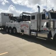 White tow truck from Johnson Towing Services towing a FedEx trailer on a cloudy day.