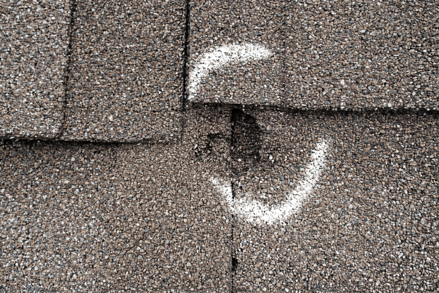 Hail damaged roof shingle with chalk marking showing impact point on an Ogden roof