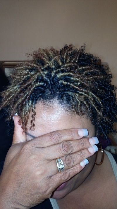 A woman with dreadlocks is covering her face with her hand.