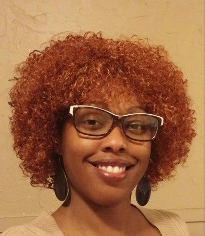 A woman with red curly hair and glasses is smiling