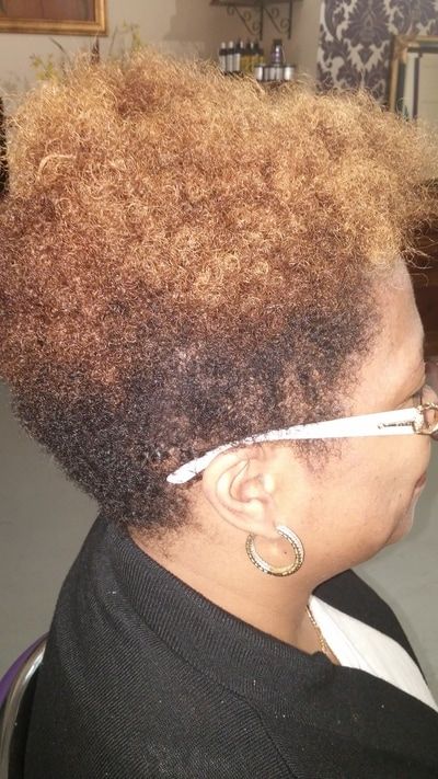 A woman with curly hair and glasses is sitting in a chair.