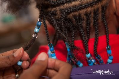 A woman is braiding a child 's hair with blue beads.