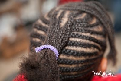 A close up of a person 's braided hair with a purple rubber band in it.