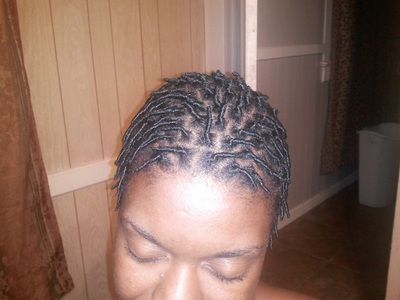 A woman with dreadlocks is standing in front of a wooden wall.