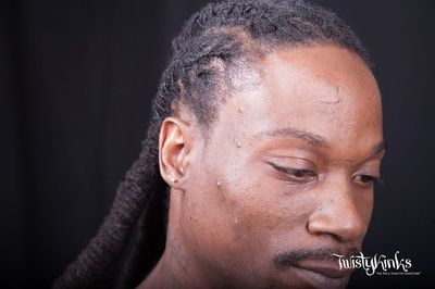 A close up of a man 's face with dreadlocks and a tattoo on his forehead.