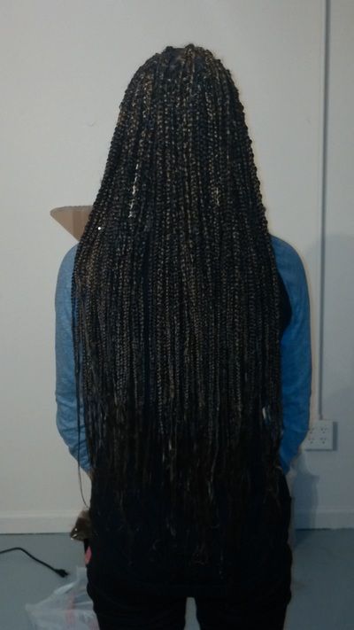 A woman with long braids is standing in front of a white wall.