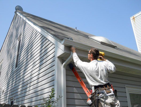 An experienced worker repairs a damaged gutter on a residential building.