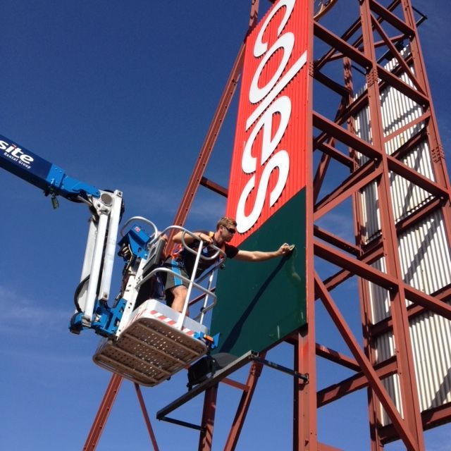 A coles sign is being installed on a tall building