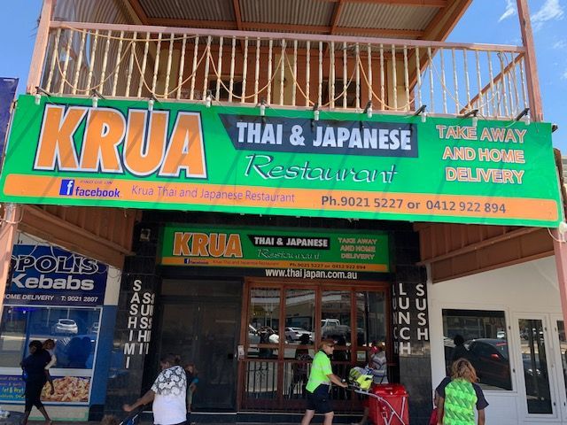 A group of people are walking in front of a thai and japanese restaurant.