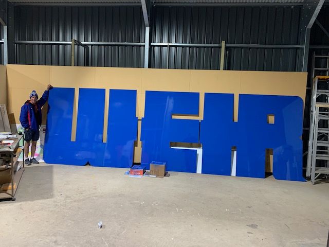 A man is standing next to a large blue sign that says weha