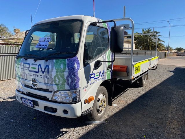 A white truck with the word rem on it is parked on the side of the road.