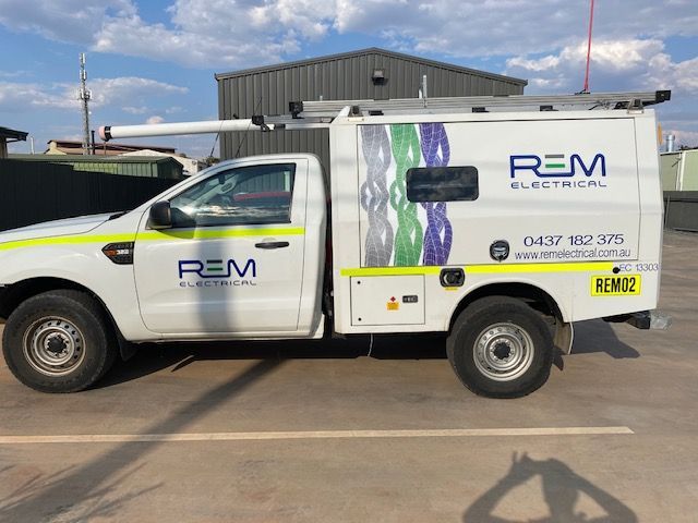 A white truck with rem electrical written on the side is parked in a parking lot.