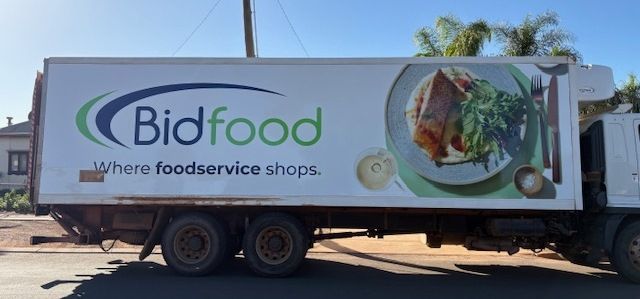 Bidfood food truck parked on a street; a white trailer with the company logo and a food graphic is visible.