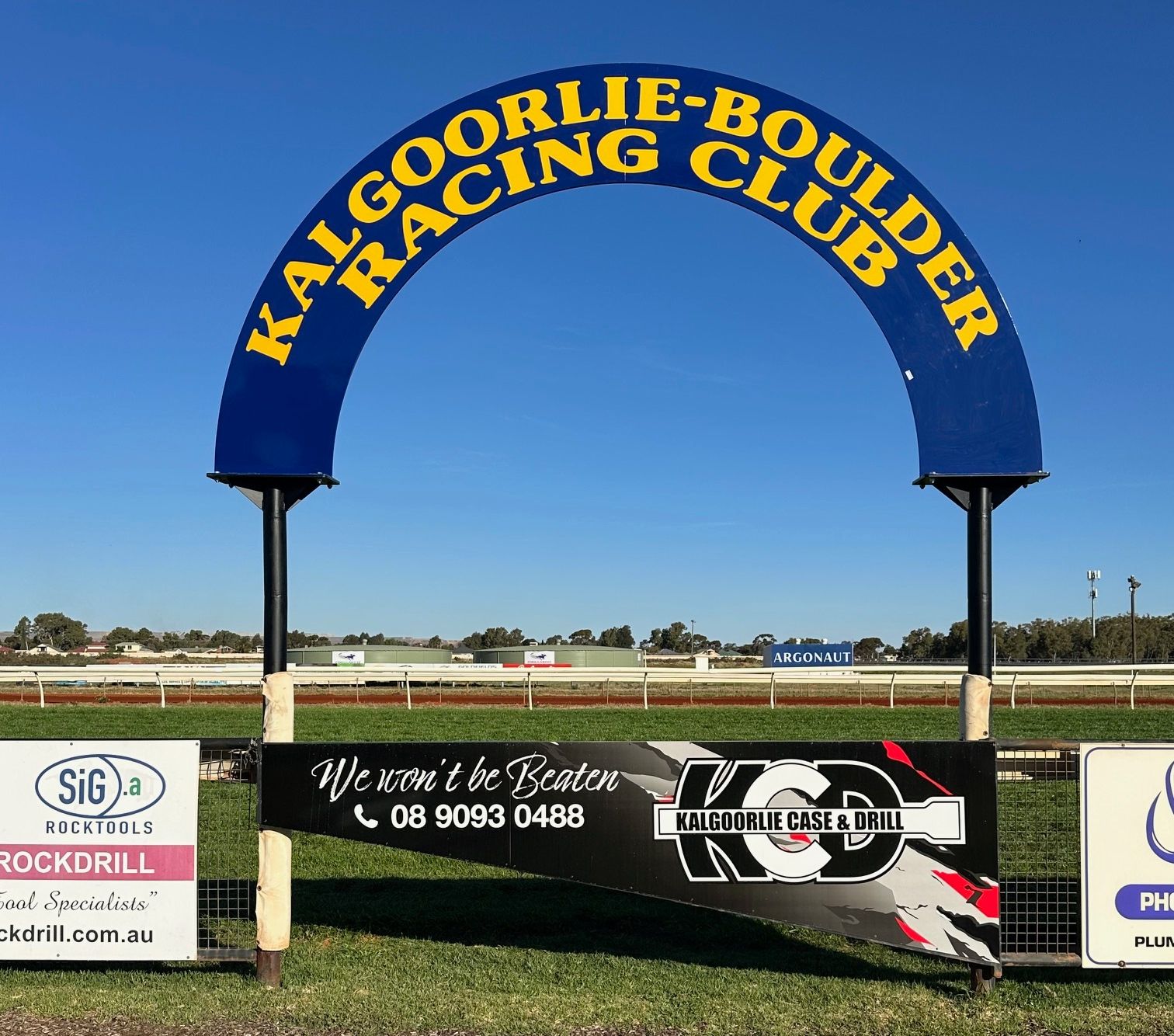 Archway at Kalgoorlie-Boulder Racing Club with text, sponsors’ signs, and a race track under a blue sky.