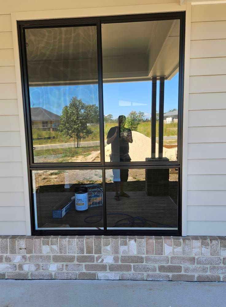 A Man is Taking a Picture of Himself in a Window of a House — PJ Tinting In Laurieton, NSW