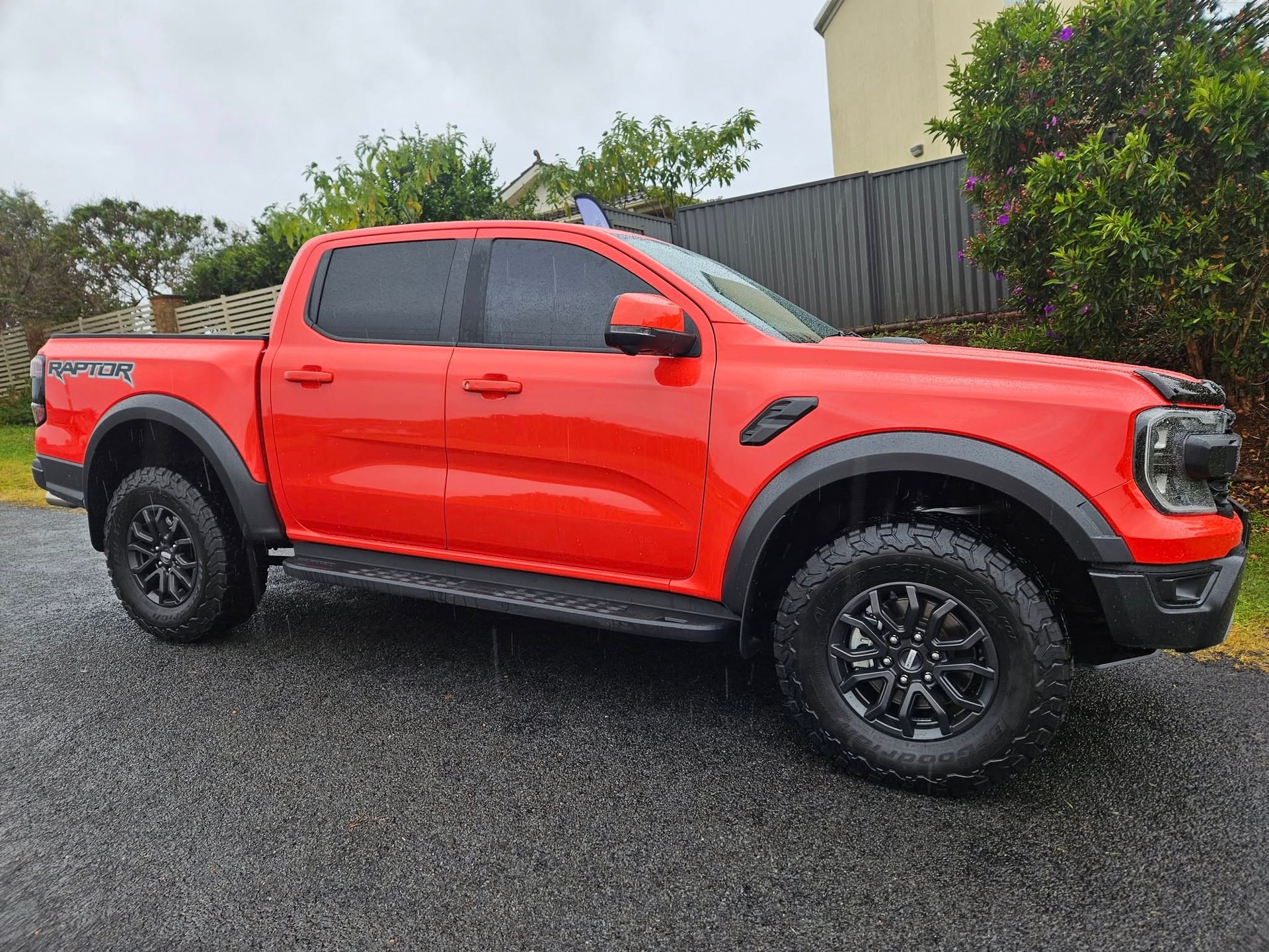 Bright orange Ford Ranger Raptor pickup truck parked on wet pavement.