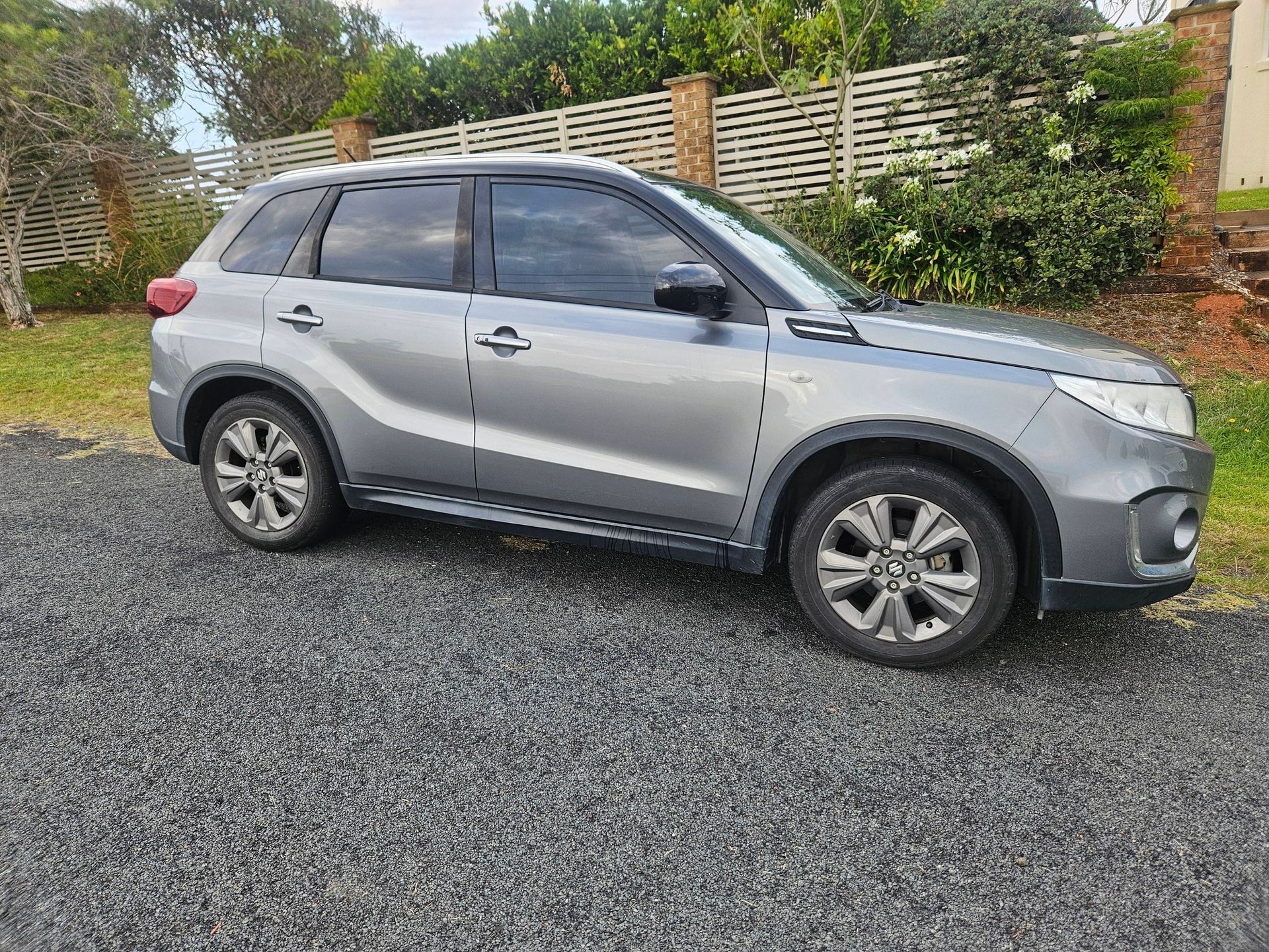 Gray Suzuki SUV parked on gravel driveway.