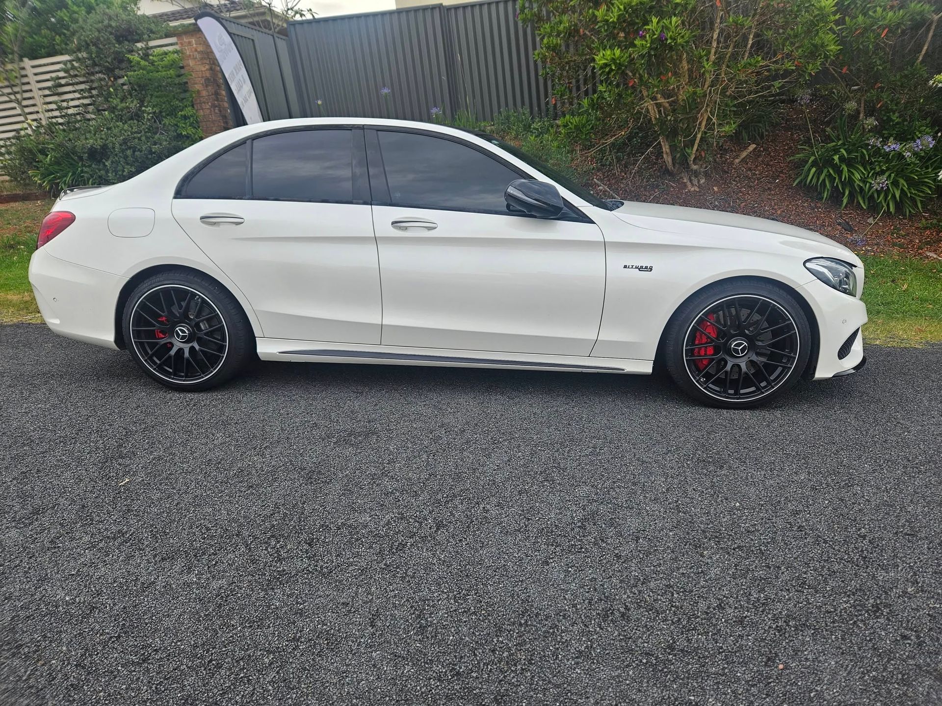 White Mercedes-Benz sedan parked on gravel with tinted windows, black rims, and red brake calipers.