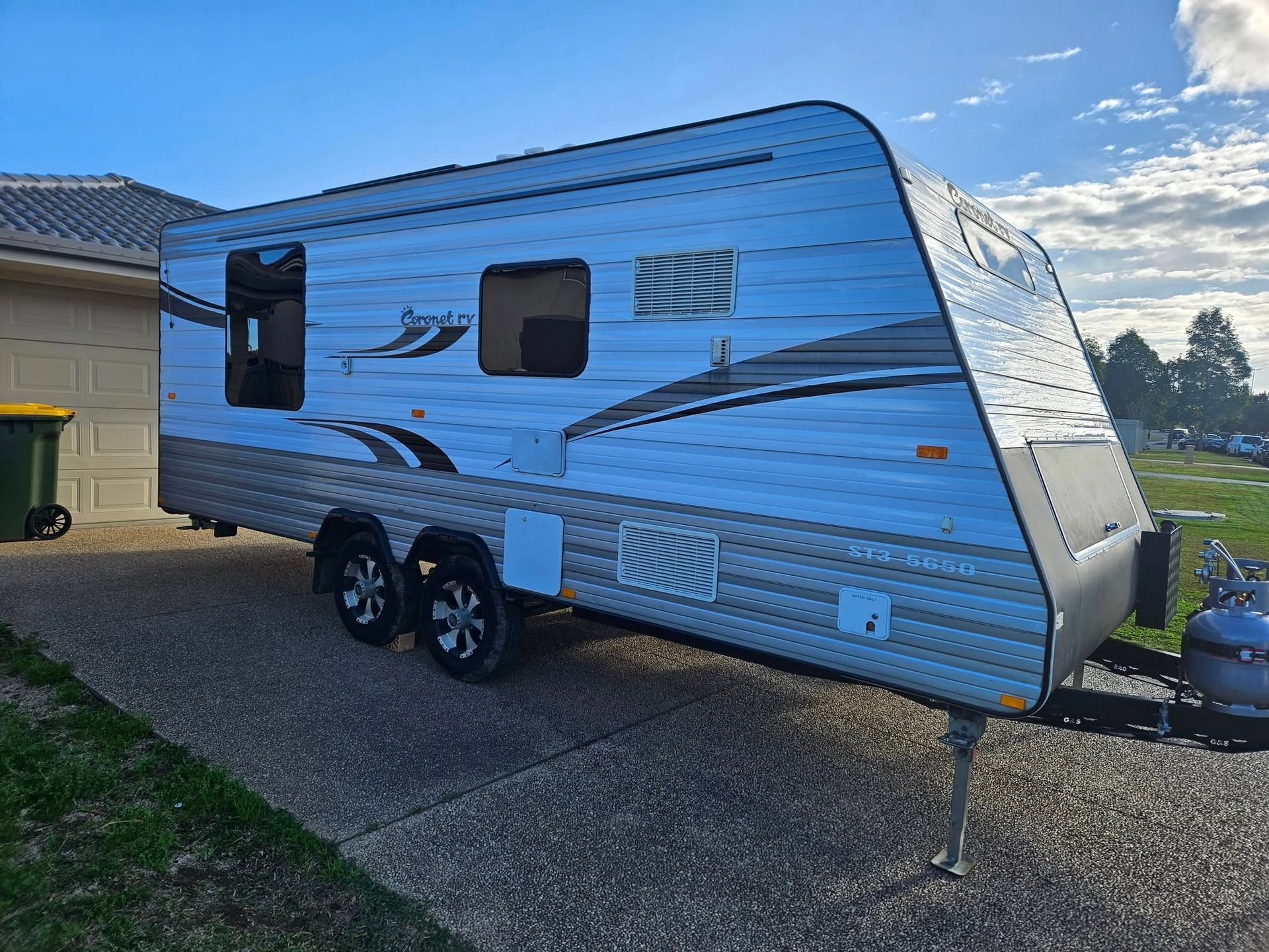 Gray and white caravan parked on a driveway with a cloudy sky in the background.