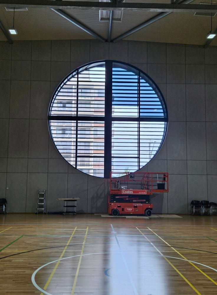 Basketball court interior with large circular window; lift in front.
