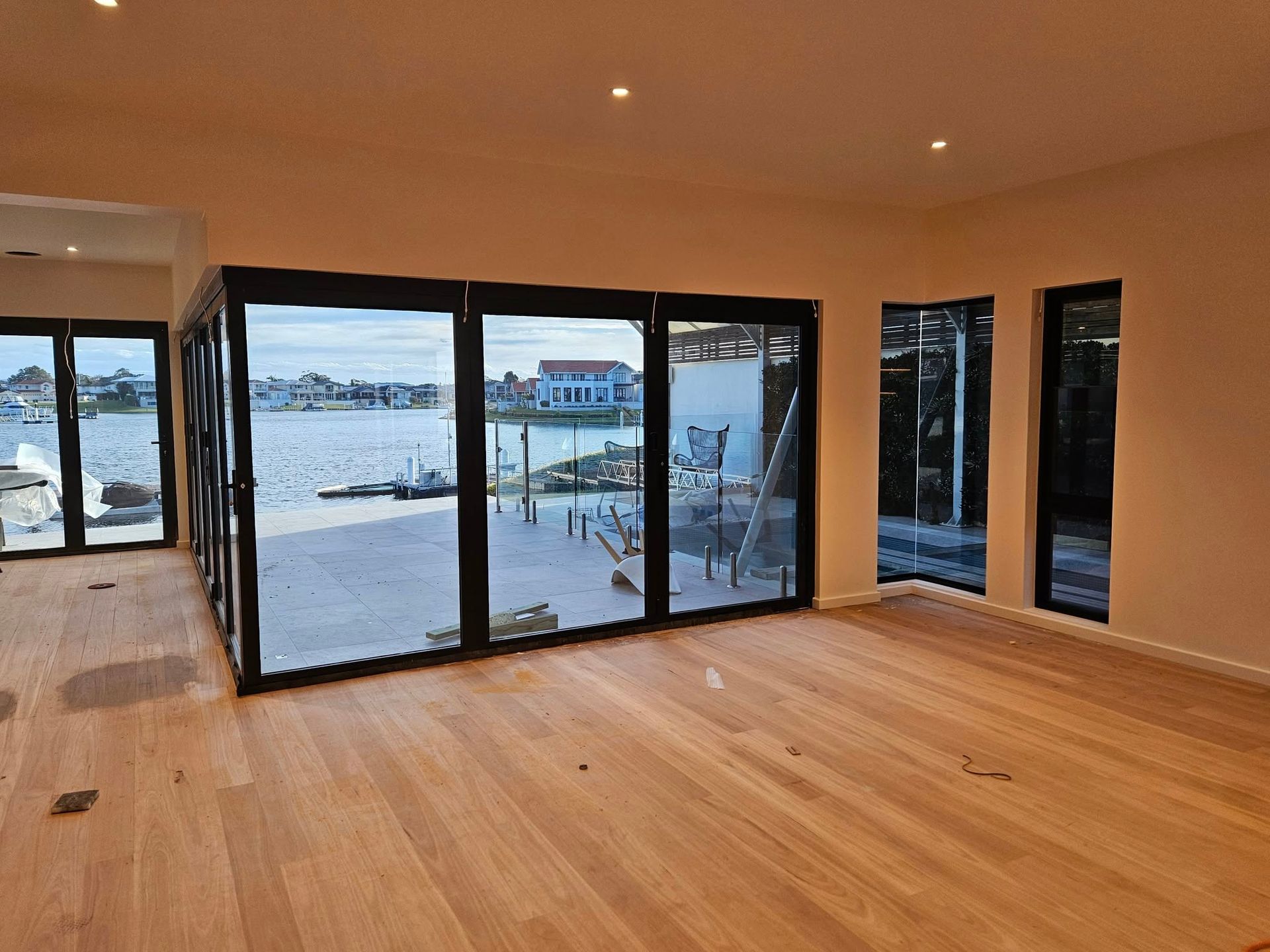 Interior of a modern room with large windows overlooking water and wooden flooring.