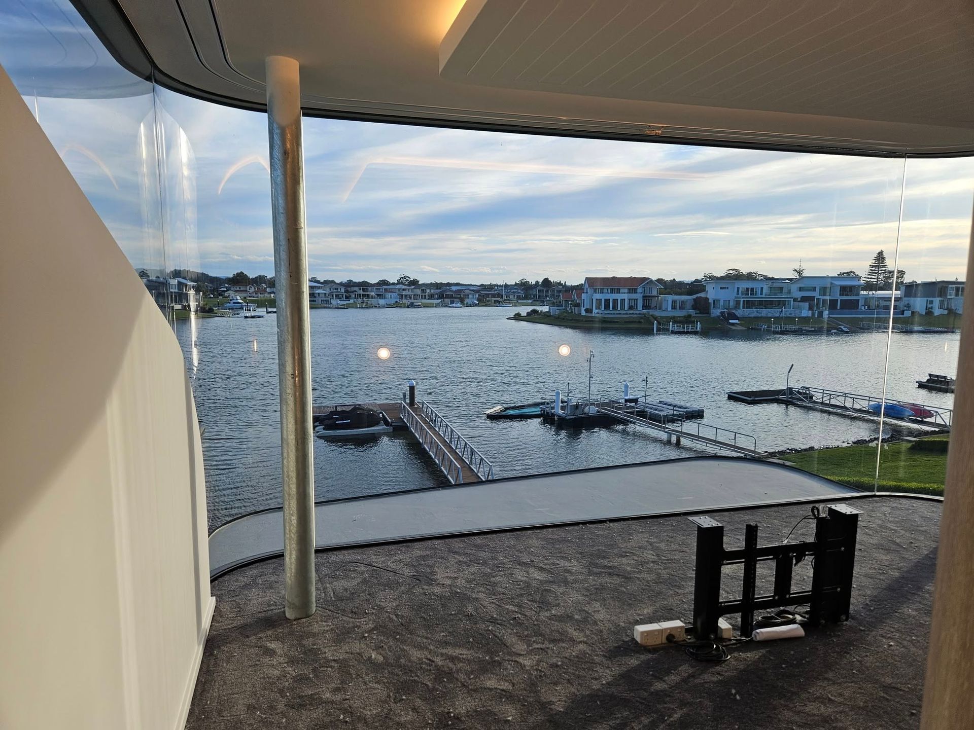 View of a lake with houses, docks, and boats from a modern building with a glass wall.