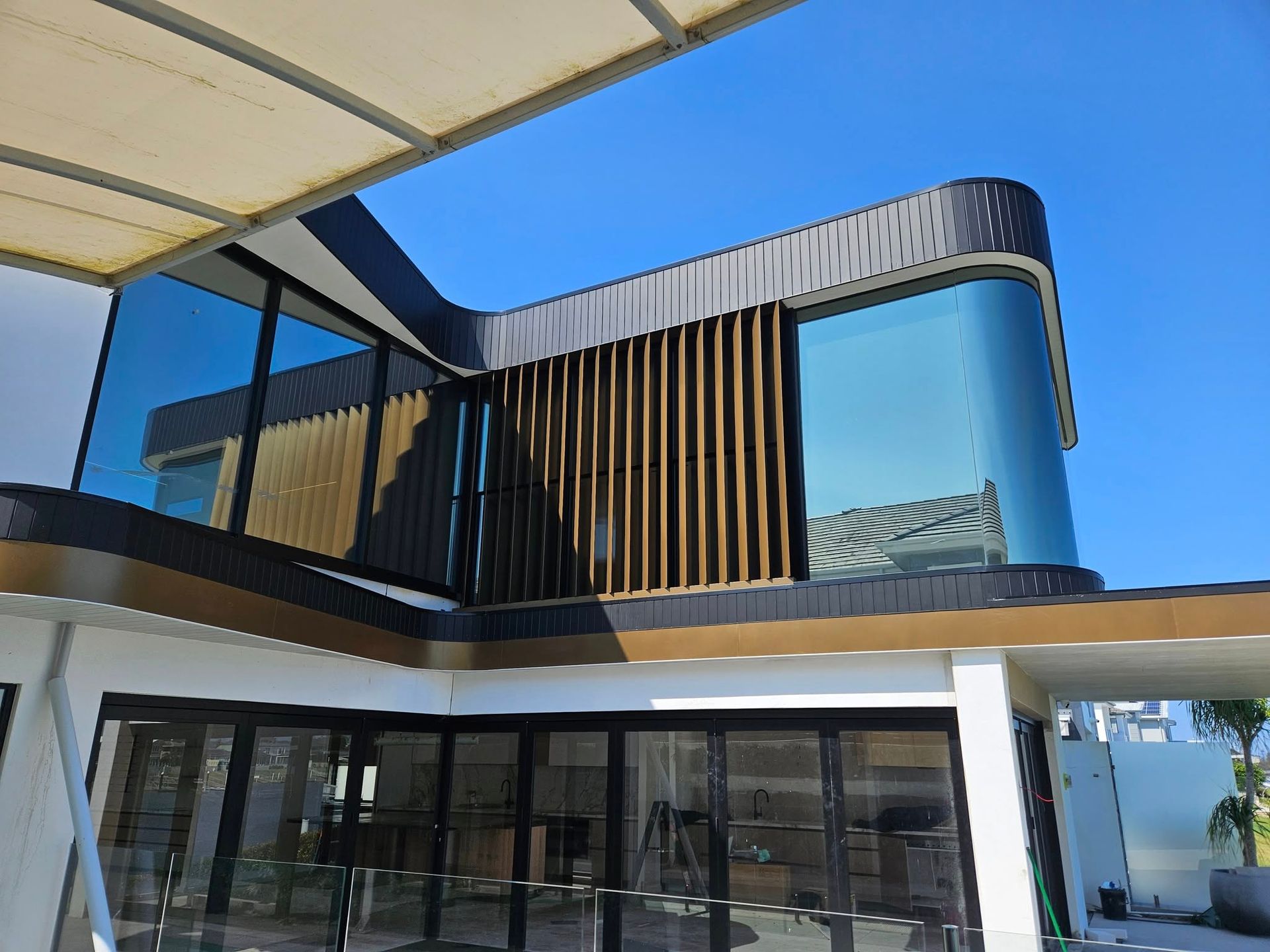 Modern building exterior with large windows, wooden slats, and curved black trim against a blue sky.