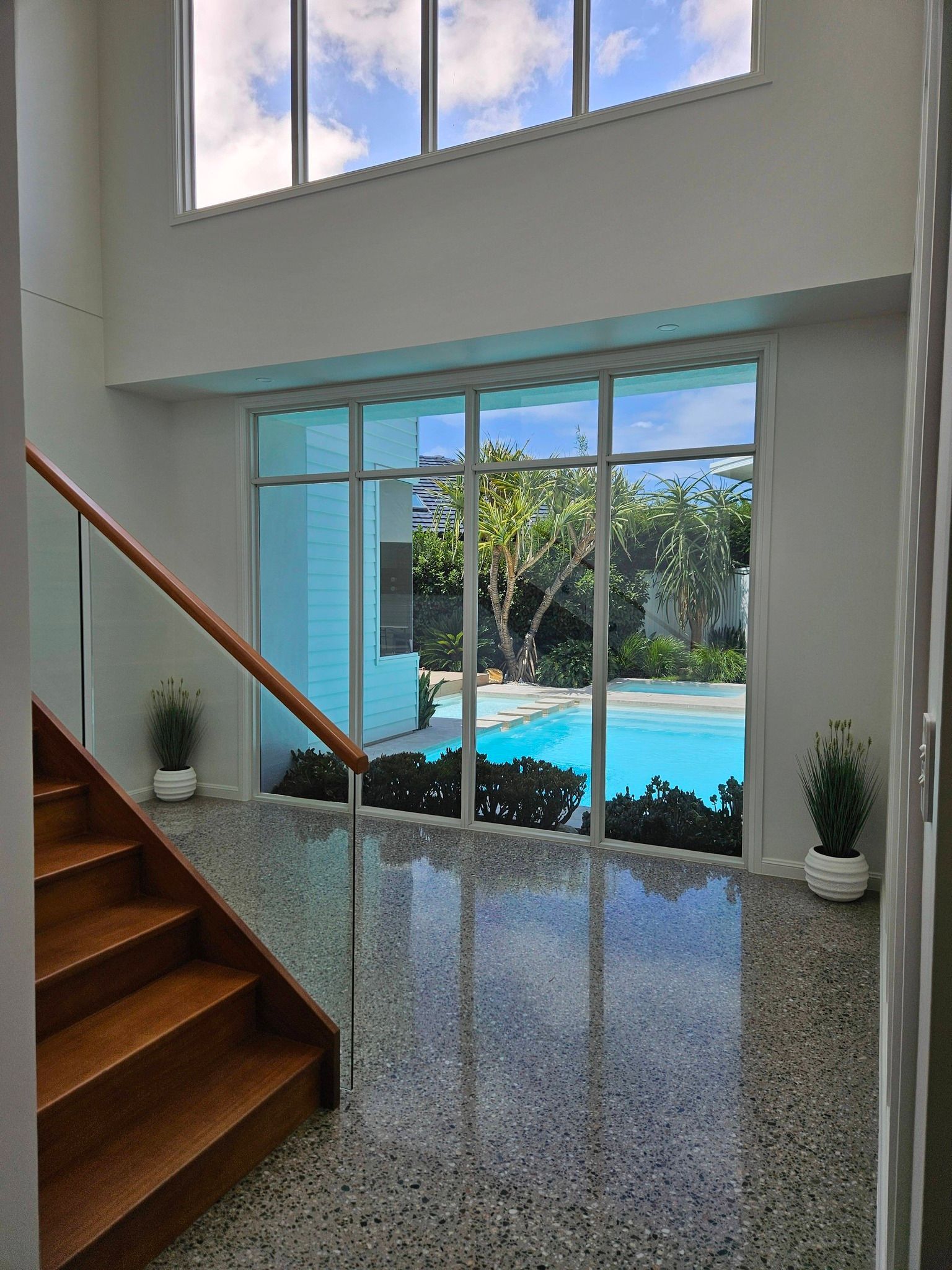 Staircase leading to a large window overlooking a pool. The floor is speckled grey, with potted plants.