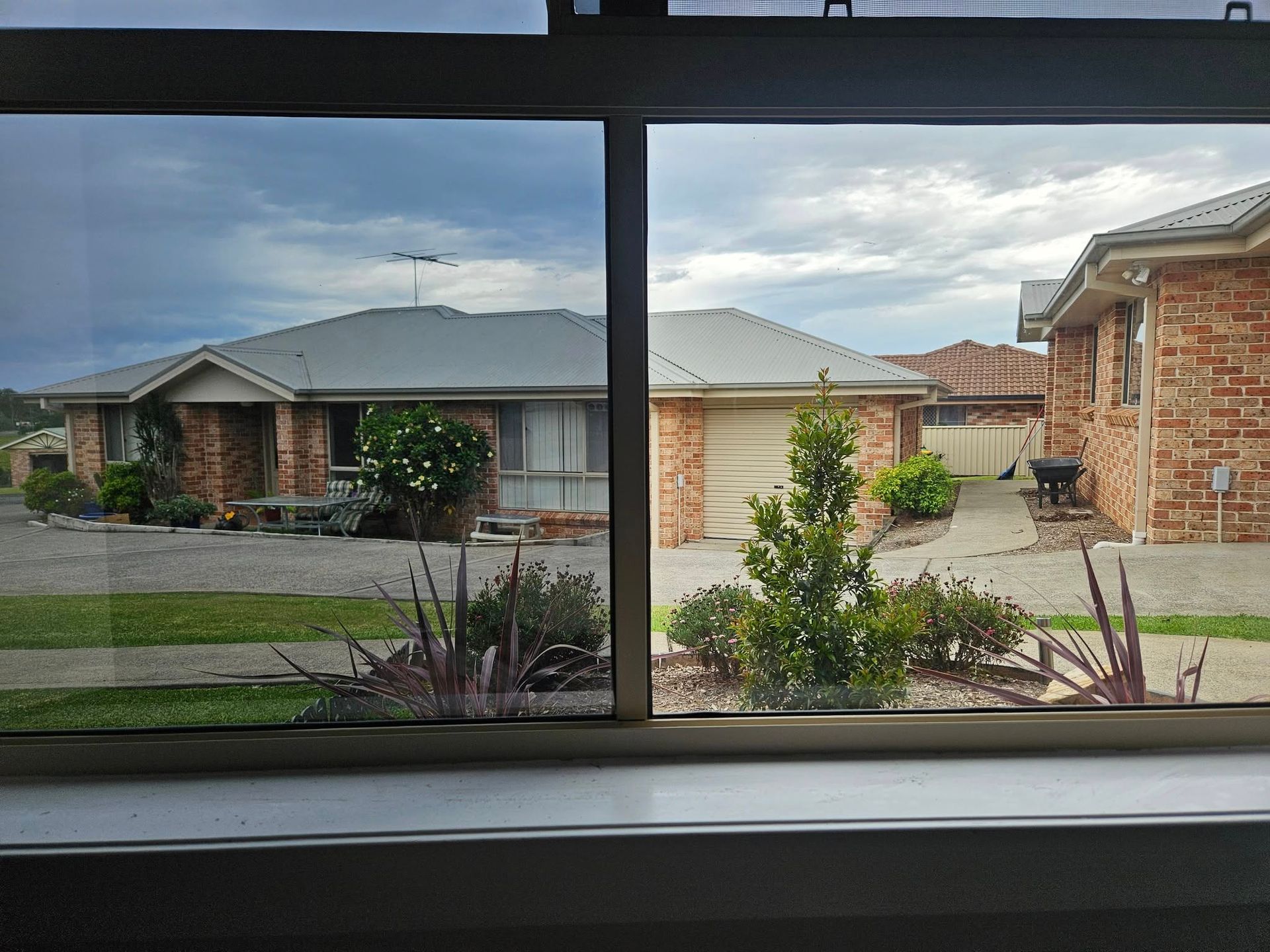 View through a window of brick houses with trees and a cloudy sky.