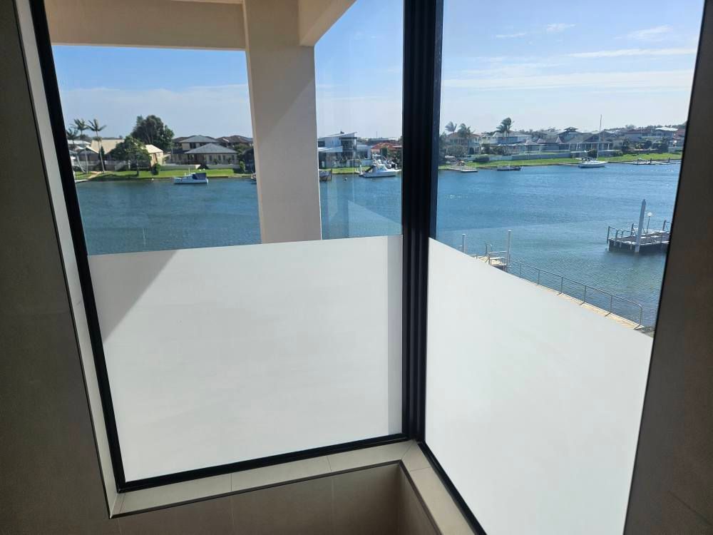 Interior view of window overlooking waterfront homes and boats on a sunny day. White window film.