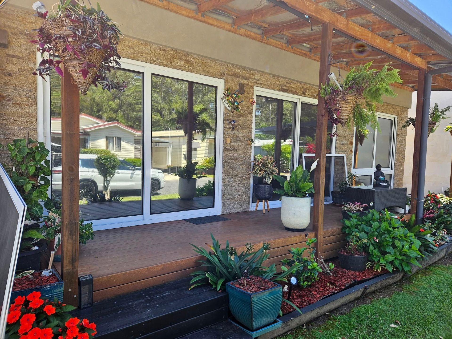 A modern home's porch with plants. Large windows reflect a car. Red and green plants surround the porch.