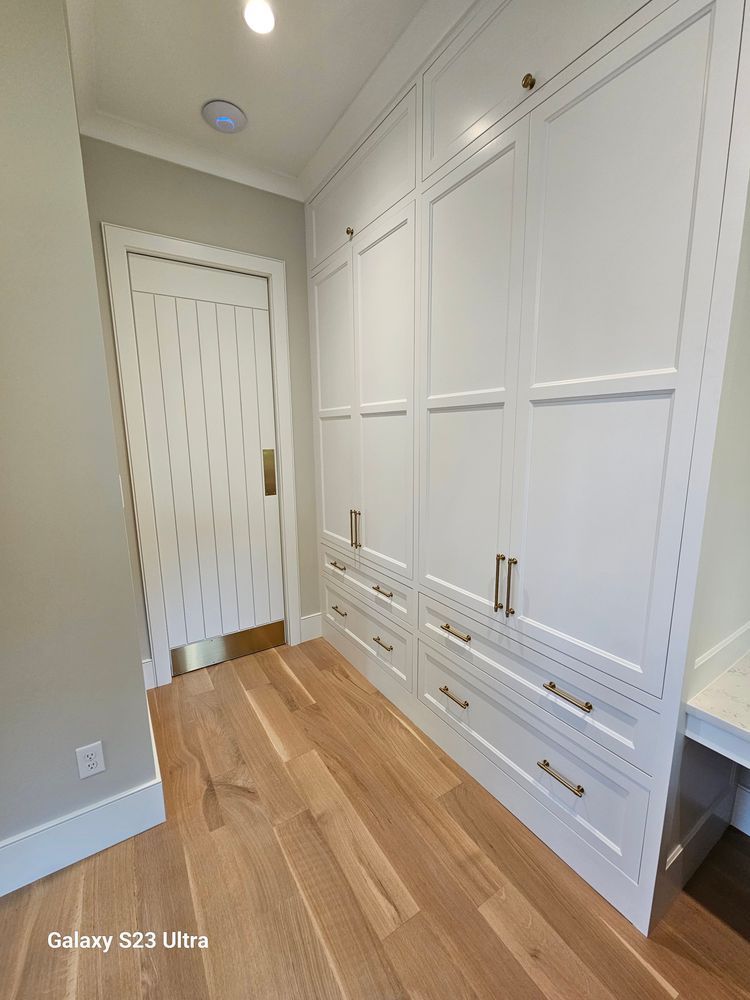 A hallway with white cabinets and drawers and a door.