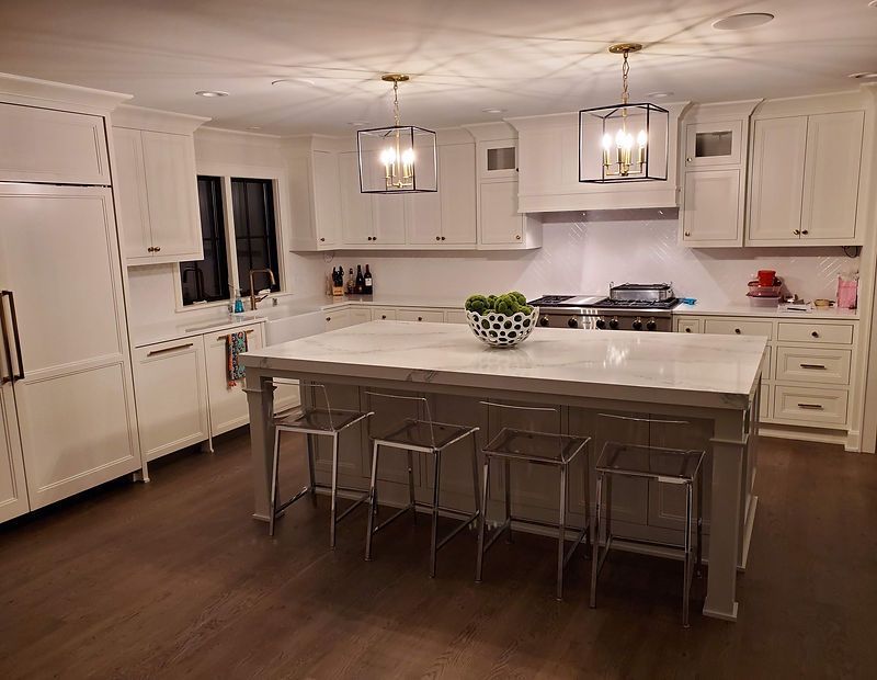 A kitchen with white cabinets , a large island , stools and a stove.