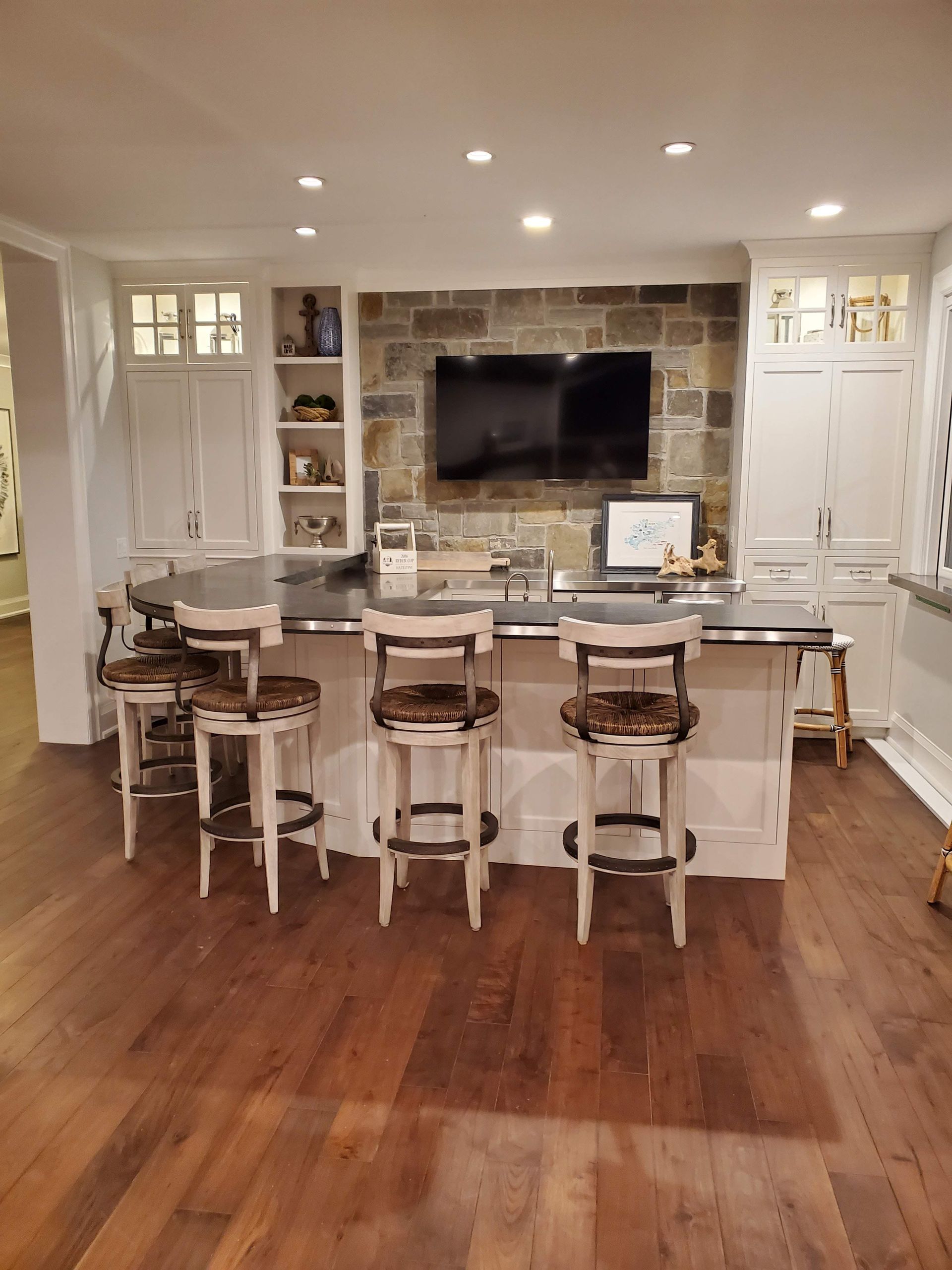 A kitchen with a large island and stools and a flat screen tv on the wall.